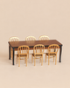 A Maileg Dining Room Set featuring a long table with a dark wood top and black legs, surrounded by six gold chairs.