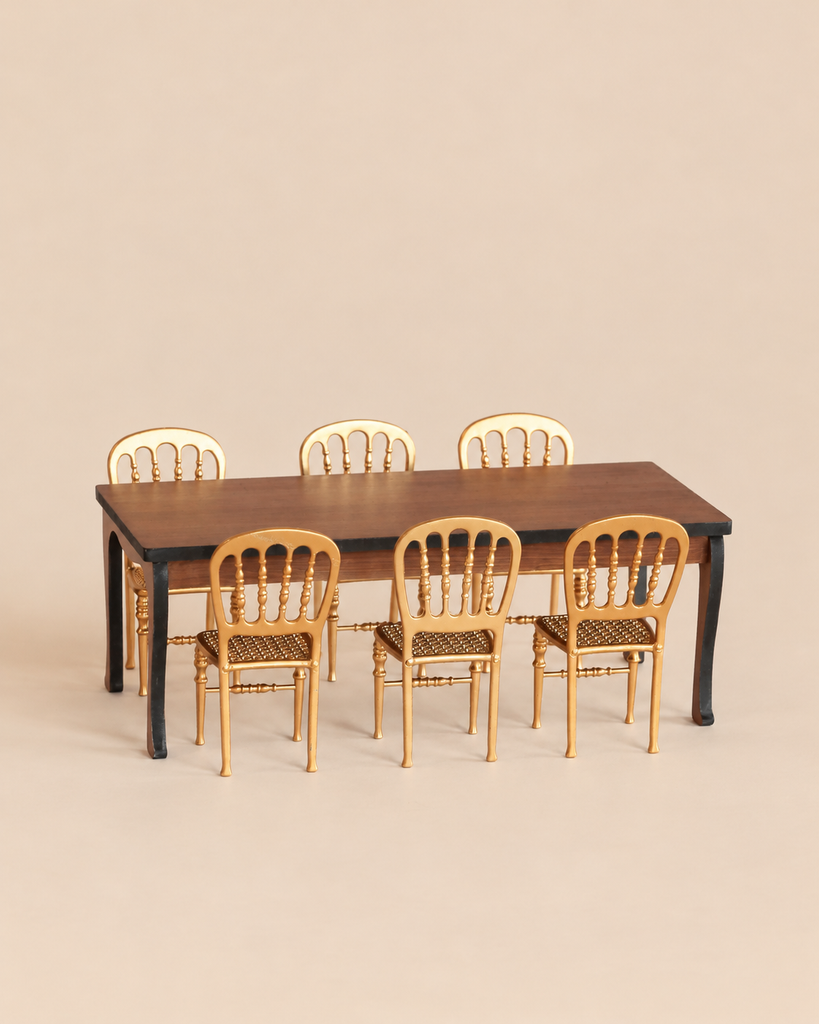 A Maileg Dining Room Set featuring a long table with a dark wood top and black legs, surrounded by six gold chairs.