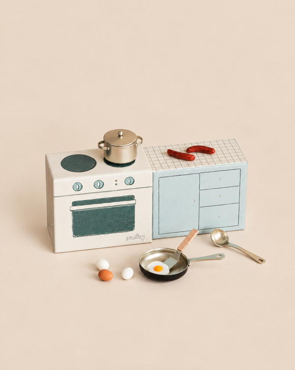Maileg Cooking Bundle, Mouse, featuring a miniature play kitchen with stove and cupboards, a metal pot, two sausages, a frying pan with a fried egg and spatula, a spoon, and three small eggs.