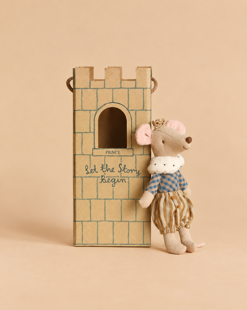 A Maileg Prince Mouse, Big Brother, is a cotton plush mouse wearing a gold crown, blue plaid shirt, and striped pants, leaning against a castle toy box labeled “Let the Story Begin.”