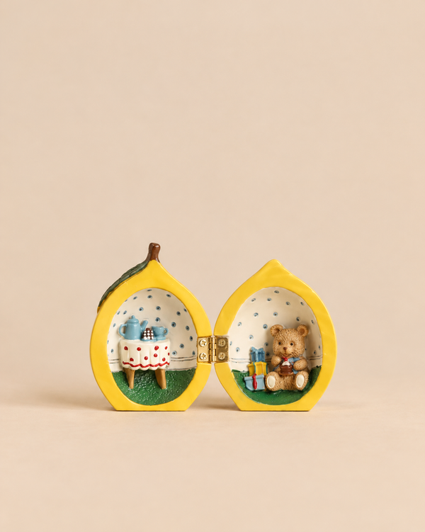 The Konges Sloejd Mini Surprise House - Lemon is a hinged ornament that opens to reveal a miniature world with a tea table on one side and a teddy bear with gifts on the other.