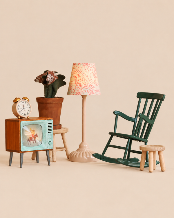 The Maileg Family Room Set includes a vintage-style television, an alarm clock, a potted plant on a stool, a floor lamp with a patterned shade, and a dark green rocking chair next to a small wooden stool.