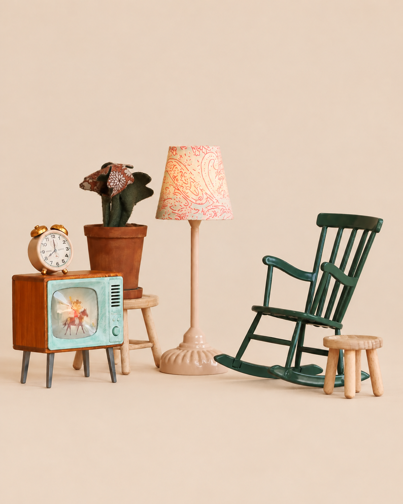 The Maileg Family Room Set includes a vintage-style television, an alarm clock, a potted plant on a stool, a floor lamp with a patterned shade, and a dark green rocking chair next to a small wooden stool.