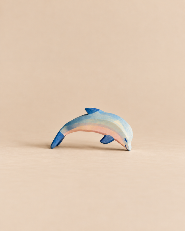 An Ostheimer Dolphin, Head Low wooden toy painted in shades of blue and pink, positioned with its head pointed downward.