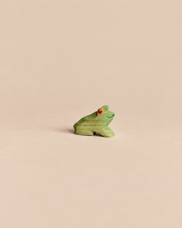 Ostheimer Frog Sitting, a small handcrafted wooden frog in a seated position with a green body and a red eye.
