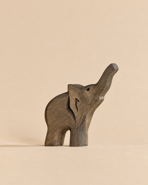 A sustainable wooden Handmade Holzwald Baby Elephant figurine with its trunk raised, perfect for imaginative play.