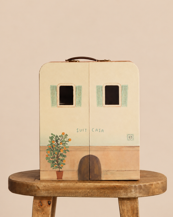 A closed, rectangular Maileg SuitCasa designed as a small building with painted windows, an orange tree, and an arched door, sitting on a wooden stool.