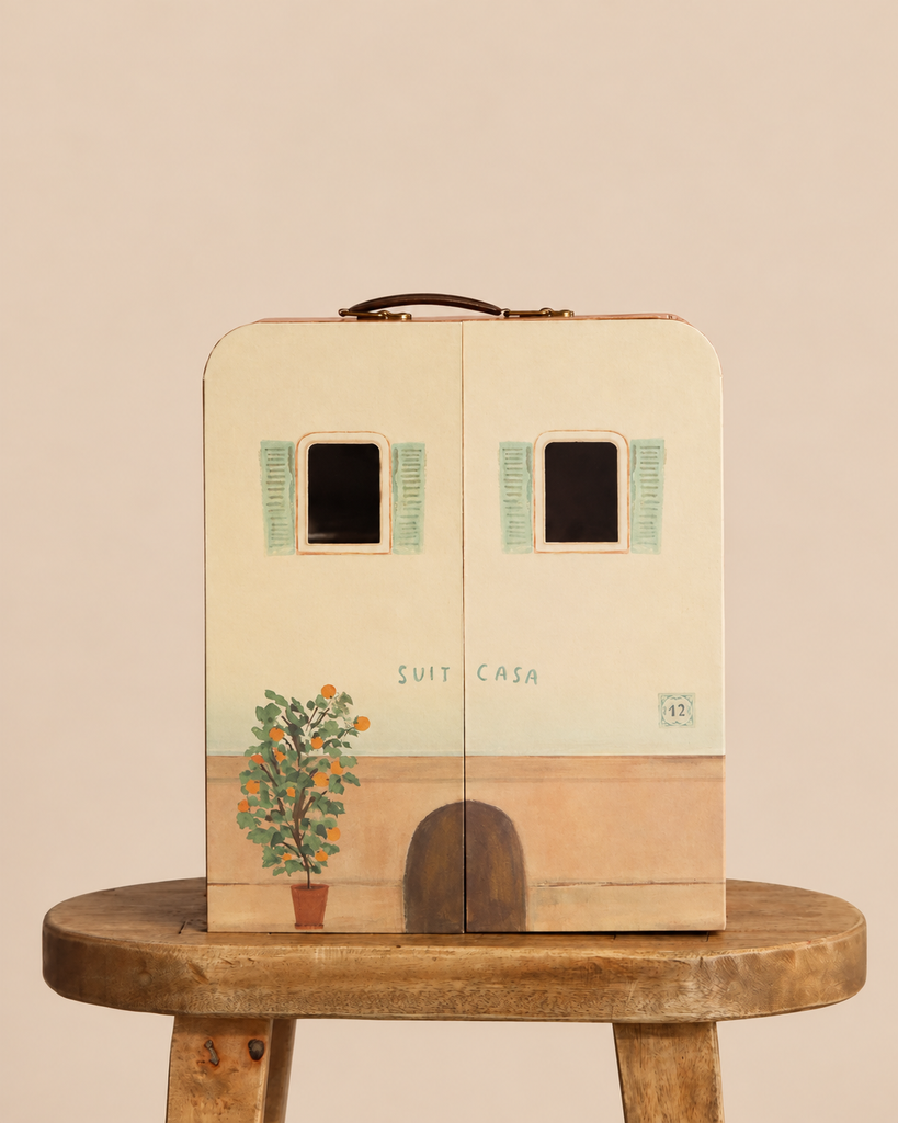A closed, rectangular Maileg SuitCasa designed as a small building with painted windows, an orange tree, and an arched door, sitting on a wooden stool.
