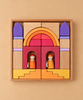Wooden blocks in shades of yellow, orange, red, and purple arranged in a wooden tray to form an arched gateway with two small wooden peg dolls inside, part of a Grimm’s Building World - Desert Sand set for imaginative play.