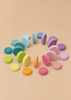 A circular arrangement of Grimm’s Wooden Pastel Coins and stacking rollers in a flat gradient.