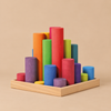 Grimm’s Large Building Rollers Rainbow set of rainbow-colored wooden stacking cylinders of varying heights standing upright in a shallow wooden tray.