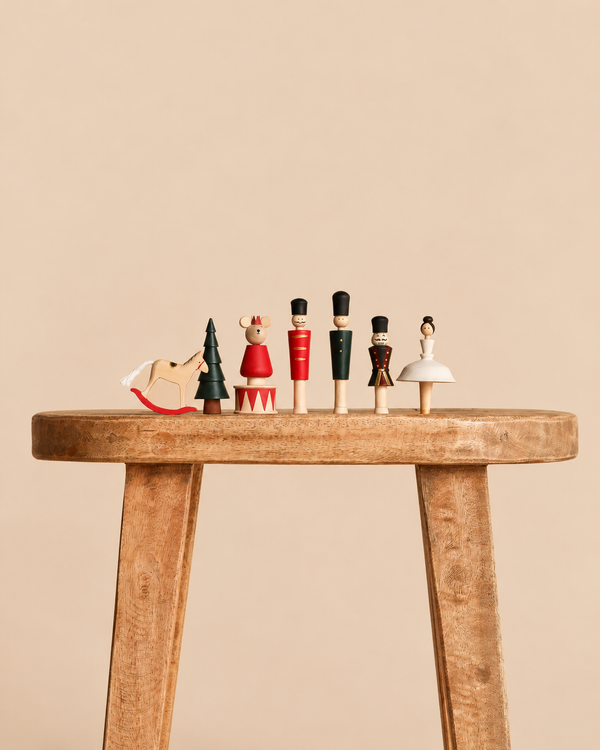 A row of six Sabo Concept Wooden Nutcracker Figurines, including a rocking horse, a tree, and several characters, standing on a wooden stool.