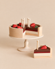 Sabo Concept Handmade Chocolate Layer Cake On A Stand featuring a wooden cake with strawberries and candles, displayed on a pedestal stand with one slice removed and placed in front.