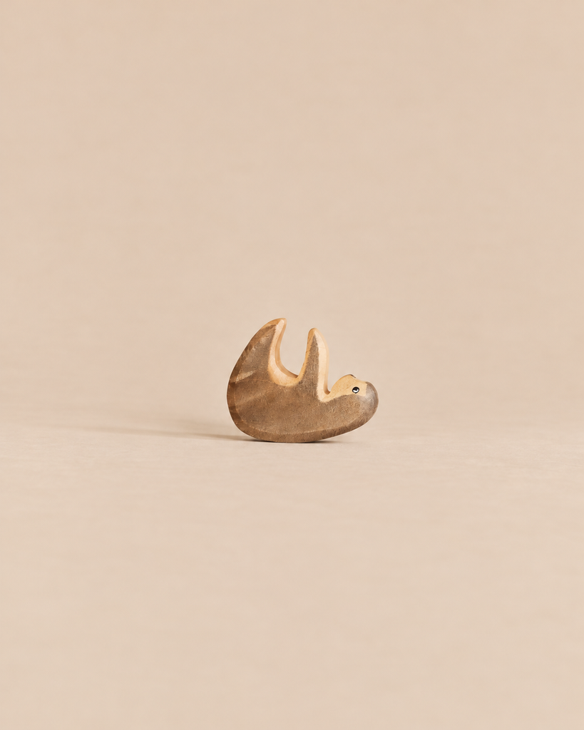 A small, sustainable Handmade Holzwald Small Sloth wooden figurine hanging from a branch.
