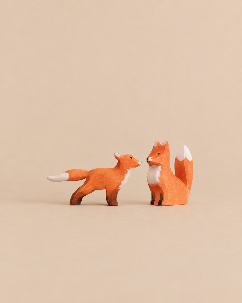 A Bumbu Handmade Wooden Fox Set featuring two hand-carved foxes, one standing and one sitting, facing each other as educational animal figures.