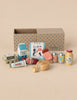 Maileg Miniature Grocery Box containing a carton of milk, a tub of ice cream, a popsicle, a jar of honey, canned drinks, a carton of eggs, a tube of mayonnaise, a sausage, and a round cheese, displayed in front of a blue-dotted cardboard box.