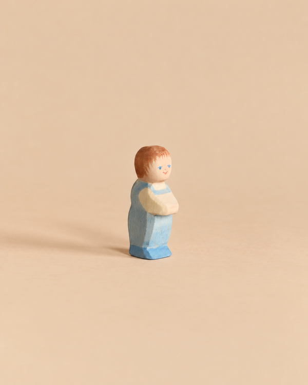 A small handcrafted Ostheimer Toddler wooden figurine of a toddler wearing a blue outfit.