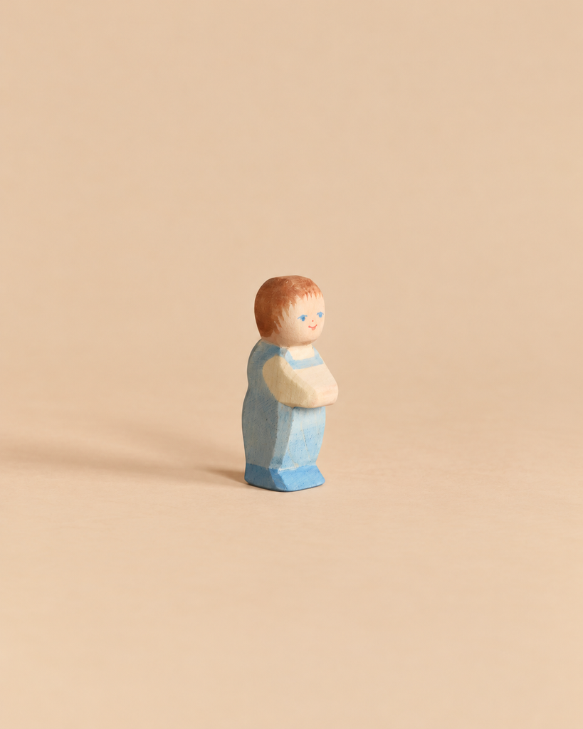 A small handcrafted Ostheimer Toddler wooden figurine of a toddler wearing a blue outfit.