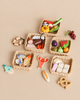 Four Market Baskets filled with wooden play food, including various fruits, vegetables, fish, meats, and breads, arranged on a tan surface.