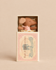 A Maileg Sleepy Wakey Baby Mouse in Matchbox - Rose featuring a small brown mouse with a pink bow, tucked into a soft fabric bed inside a decorative matchbox.