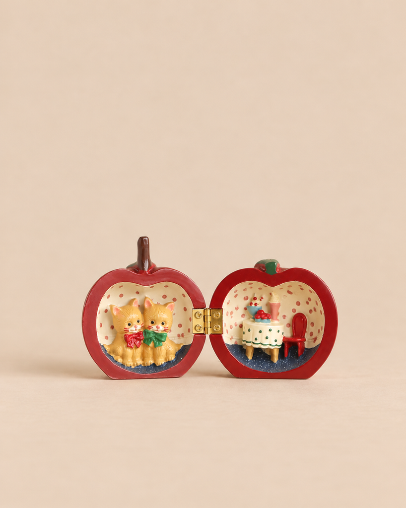 Konges Sloejd Mini Surprise House - Cherry, an open apple-shaped trinket box featuring a miniature world with two kittens on one side and a dining table with a chair on the other.