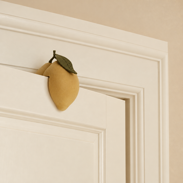 A yellow, lemon-shaped Konges Sloejd Door Stopper - Lemon with a green leaf perched on the top edge of a door.