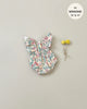 A Minikane | Lou Romper in Bohemian Bunny Doll Clothing, crafted from printed cotton, designed to fit 13" and 14" Minikane Gordis dolls, is displayed on a light grey background. To the right of the romper, two yellow billy ball flowers are tied together with string.