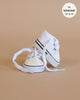 A pair of Minikane Doll Shoes | Converse Style White Sneakers with black stripes, laces untied, is displayed against a beige background. An inset circle in the top right corner reads “fits Minikane Gordis 13’’ & 14’’.”