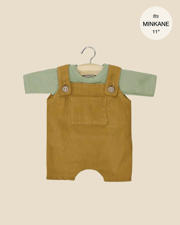 The Minikane Doll Clothing set, ideal for baby dolls, includes a green jersey short-sleeved t-shirt paired with khaki overalls. It features buttons and a front pocket, and the size is labeled "fits MINKANE 11".