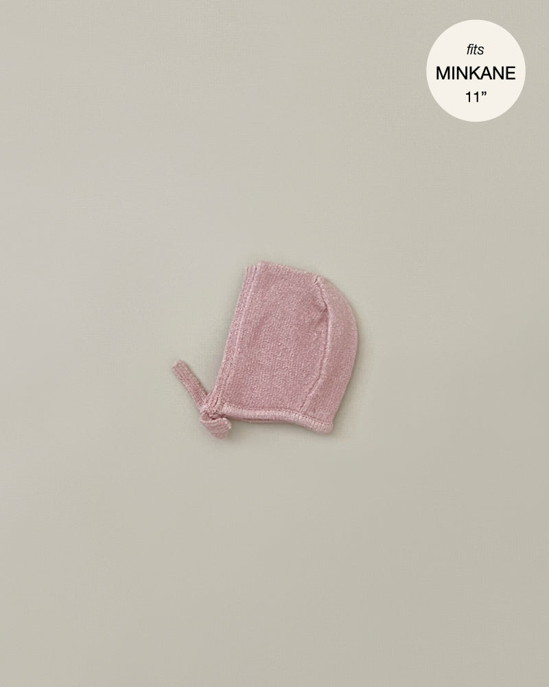 A small pink knitted bonnet, perfect for Minikane Babies, is displayed on a plain light gray background. The text "fits MINKANE 11"" is shown in the upper right corner inside a white circle. The product name is Minikane Doll Clothing | Élie Tea Pink Knit Bonnet.