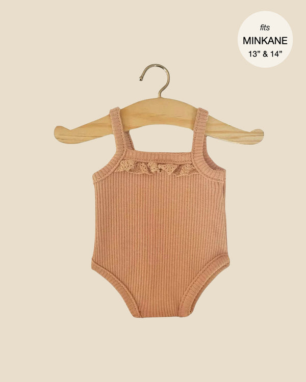 The Minikane Doll Clothing Les P'tits Basique Jumpsuit, crafted from brown sugar ribbed knit, is displayed on a wooden hanger against a light background. Designed for 13" to 14" Minikane Gordis dolls, this charming outfit features spaghetti straps and a delicate lace trim.