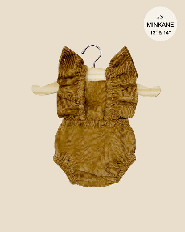 The Lou Retro Romper in brown corduroy for Minikane dolls is elegantly showcased on a wooden hanger against a simple beige background. A circular label highlights it as an essential piece among doll clothing, perfectly fitting 13" and 14" Minikane dolls. The romper, with its charming ruffled straps, ships in approximately one week.