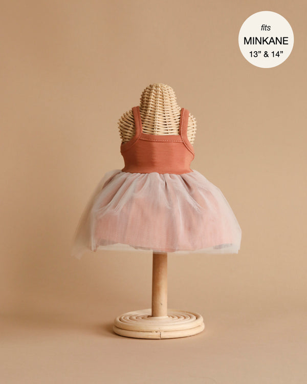 A wicker mannequin on a neutral beige background is dressed in a sleeveless rust-colored cotton top paired with the Minikane Doll Clothing Rosella Tutu, a light pink tulle skirt. A circular label in the upper right corner reads "fits MINKANE 13"" & 14"," designed in France, and hand washable.