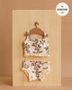 A Minikane 13" Doll Clothing | Les P'tits Basiques, 2-Piece Set in Jersey - Gisele, featuring a floral sleeveless top and ruffled bottoms, hangs on a wooden hanger. Label: fits Minikane dolls 13", made in France.