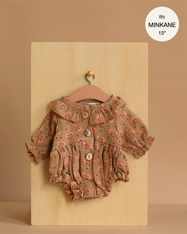 The Minikane 13" Doll Clothing | Leonore Ruffled Romper in Crepe - Eloise, featuring a brown floral pattern, ruffled collar, and buttons, is displayed on a wooden board with a small hanger. A label reads "fits Minikane Gordis dolls 13''.