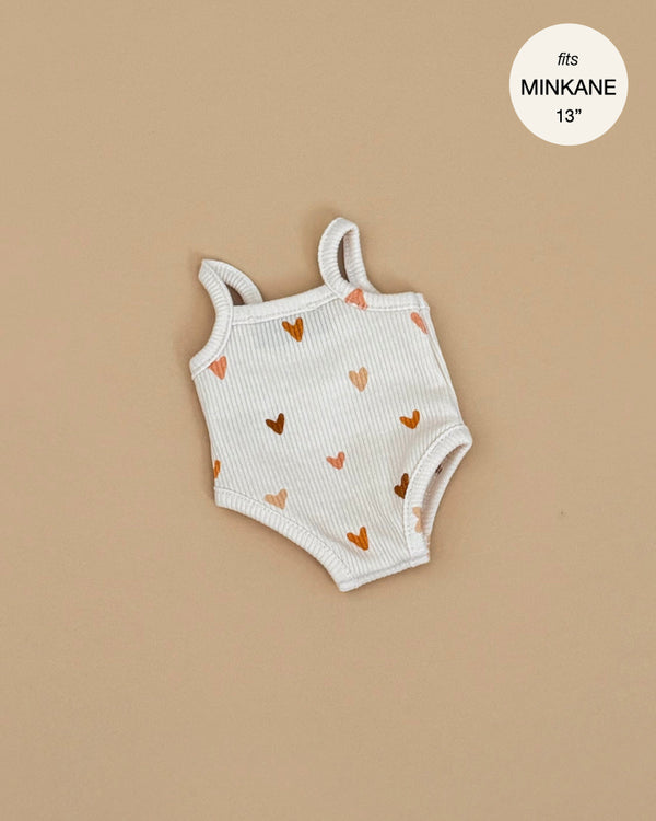 Minikane Doll Clothing | Les P'tits Basique, ribbed cotton jumpsuit in Brown Sugar Hearts for Minikane Gordis dolls, sleeveless with brown and peach heart patterns, shown flat on beige; circular label says “fits MINIKANE 13”.