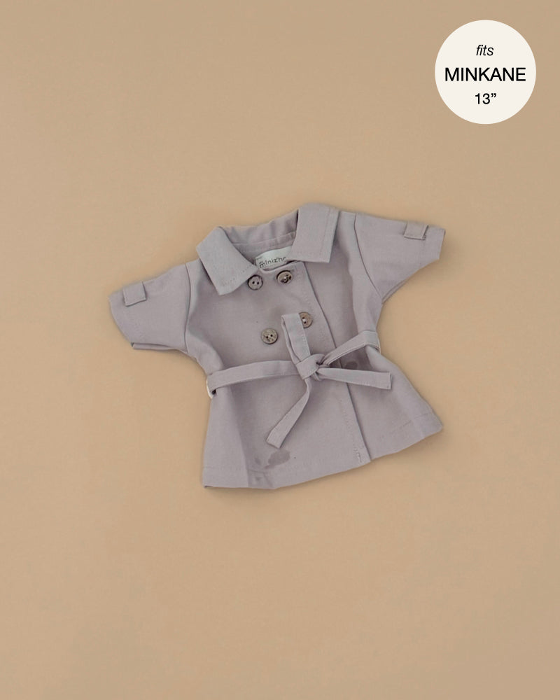 The Minikane Doll Clothing | Back to School - Tara Trench Coat in Beige Gabardine, a small double-breasted coat with a belt for Minikane or other 13" dolls, is shown on a beige background with a "fits MINIKANE 13" circular label in the top right corner.