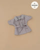 The Minikane Doll Clothing | Back to School - Tara Trench Coat in Beige Gabardine, a small double-breasted coat with a belt for Minikane or other 13" dolls, is shown on a beige background with a "fits MINIKANE 13" circular label in the top right corner.