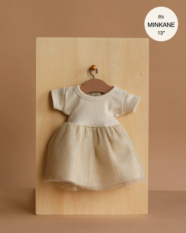 The Minikane Doll Clothing | Rosana Short Sleeve Tutu - Gold features a small cream knit dress with short sleeves and a sparkly gold tulle skirt, displayed on a wooden hanger. Designed to fit 13" Minikane dolls.