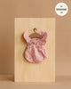 The Minikane 13" Doll Clothing | Lou Retro Romper in Cotton Gauze - Petal Pink hangs on a small wooden hanger against a light wood board, with a label stating it fits Minikane Gordis dolls 13'' on a beige background.