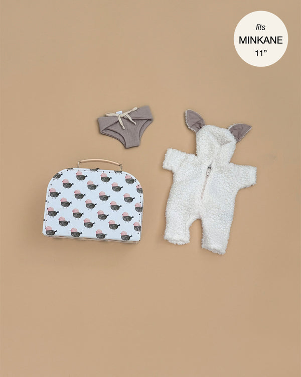 The Minikane 11" Doll Clothing | Jeannot Jumpsuit & Diaper in Suitcase Set includes a white bunny-ear hooded jumpsuit, gray bow shorts, and a sheep-patterned white suitcase, displayed on a beige background.