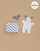 The Minikane 11" Doll Clothing | Jeannot Jumpsuit & Diaper in Suitcase Set includes a white bunny-ear hooded jumpsuit, gray bow shorts, and a sheep-patterned white suitcase, displayed on a beige background.