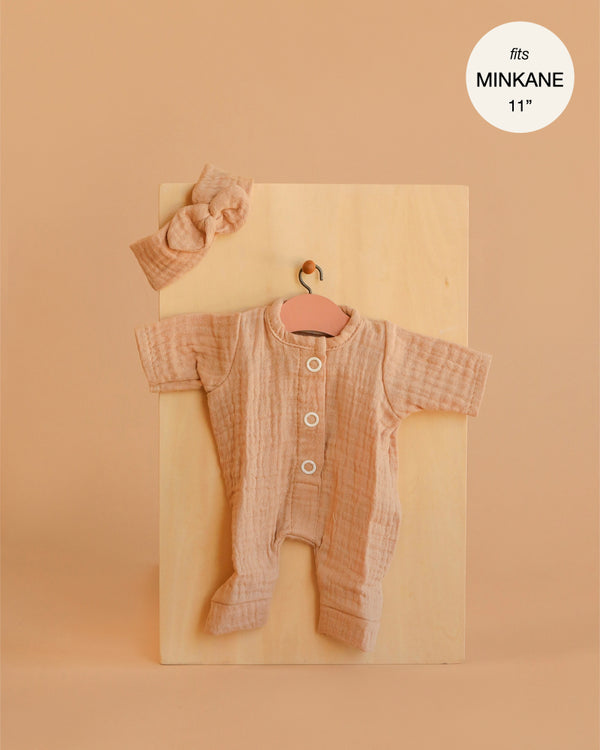The Minikane 11" Doll Clothing | Lili Jumpsuit & Headband in Cotton Gauze - Latte features a peach-toned textured jumpsuit with three white buttons and a matching headband, displayed on a wooden board—perfect for stylish doll lovers.