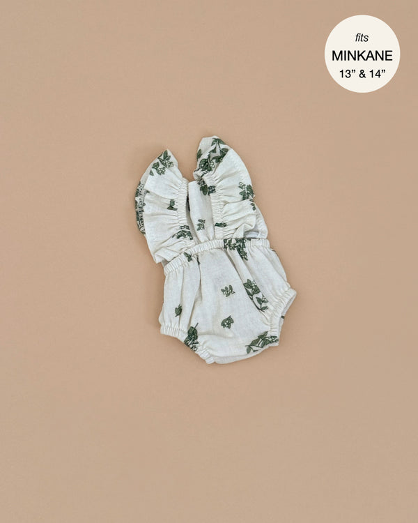The Minikane Doll Clothing Lou Retro Romper, a sleeveless romper with ruffled straps and a light gray floral pattern, is elegantly displayed on a beige background. Designed in France to fit 13" and 14" dolls, the circular tag reads "fits Minikane 13” & 14”.