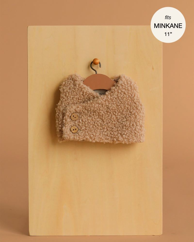 The Minikane Doll Clothing | Babies – Terry Sleeveless Vest in beige is a small, sleeveless vest with two buttons, displayed on a hanger against a tan background. Fits Minikane 11'' dolls—perfect for baby doll outfits.