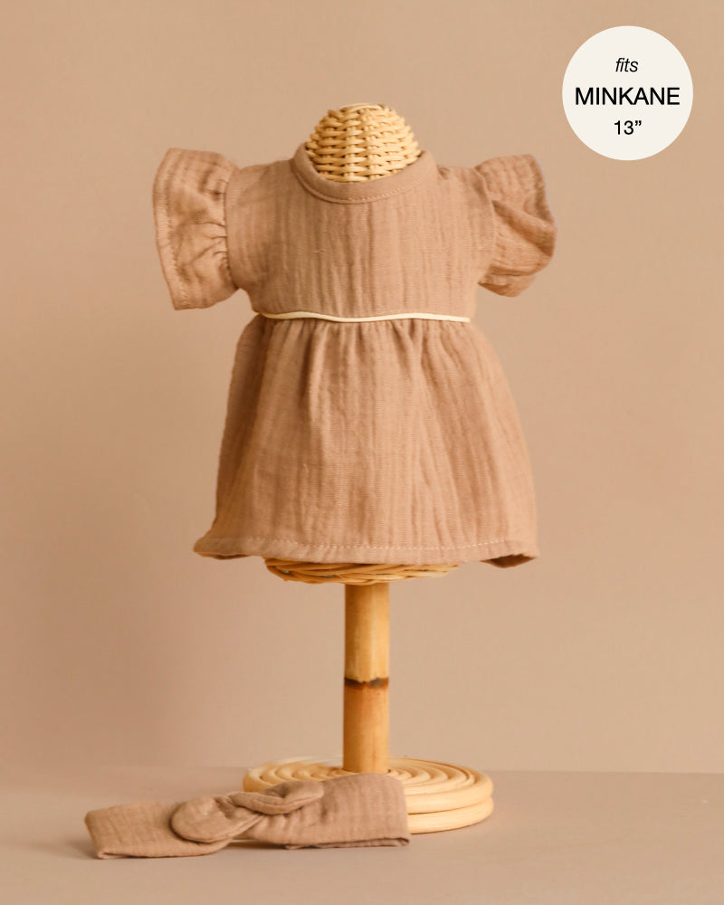 A small woven mannequin models the Minikane Doll Clothing Daisy Dress & Headband in Cotton Gauze - Latte, featuring a short sleeve ruffled dress with white trim for 13-inch dolls, perfect to enhance your 13 inch doll wardrobe.