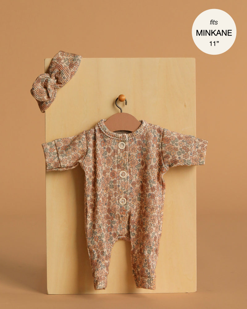 The Minikane 11" Doll Clothing | Lili Jumpsuit & Headband in Ribbed Knit - Cocoa Flowers features a floral long-sleeve knit romper with three buttons, a matching headband, and a “fits Minikane 11” label on a neutral background.