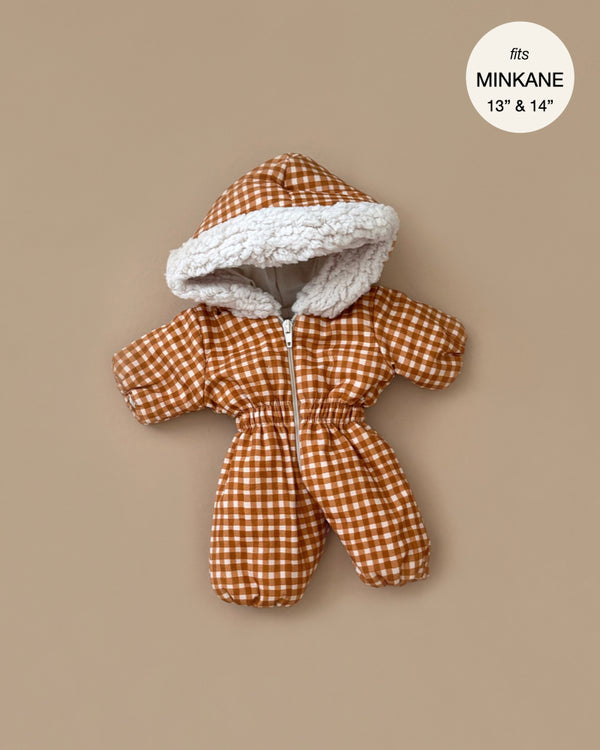 The Gigi Vichy Caramel Ski Suit, a stylish brown checkered ski suit with white fleece lining, fits Minikane dolls (13" and 14"). Elegantly displayed on a beige background, this French-made snowsuit offers warmth and charm for your beloved doll collection.