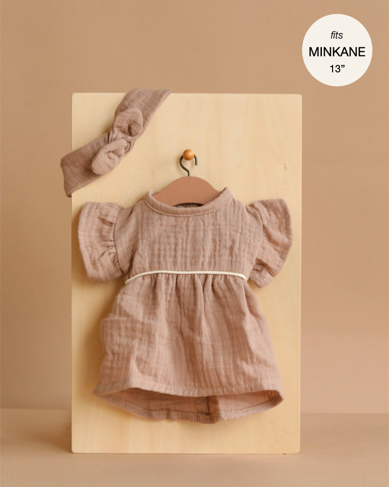The Minikane 13" Doll Clothing | Daisy Dress & Headband in Cotton Gauze - Mocha features a ruffled mocha dress with a white ribbon and matching headband, displayed on a board, and fits 13-inch or Minikane dolls perfectly.