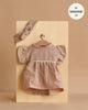 The Minikane 13" Doll Clothing | Daisy Dress & Headband in Cotton Gauze - Mocha features a ruffled mocha dress with a white ribbon and matching headband, displayed on a board, and fits 13-inch or Minikane dolls perfectly.